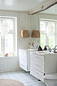 Bright, white bathroom with twin sinks against large mirror