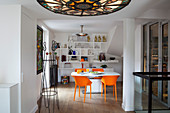 Stained-glass ceiling light and dining table with orange chairs in background