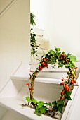 Hand-made wreath of rose hips and ivy tendrils on white wooden staircase