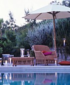 Romantic twilight ambiance: comfortable wicker armchair and lit candle lanterns next to swimming pool