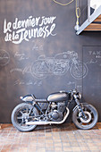 Motorbike against chalkboard wall covered in chalk drawings and writing