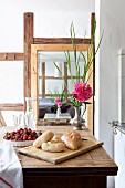 Bread rolls on chopping board, strawberries and peony on wooden table