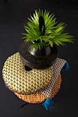 Bunt gemusterter Kissenstapel mit Ethno-Vase und grünen Blättern