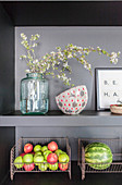 Flowering twigs and fruit in metal baskets on grey kitchen shelves