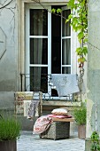 Cushions and fabrics on wicker trunk and valet stand in courtyard in front of French windows