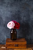 Jar of ranunculus on wooden box against black wall