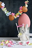 Fabric rabbit below garland of threaded paper flowers and eggs