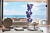 Vertical flower arrangement in living room with view of sea through panoramic window