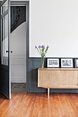 Sideboard mit schwarz-weissen Fotos und Blume vor grau-blauer Vertäfelung im Sockelbereich