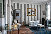 White, free-standing bathtub, gilt picture frame, ornaments and striped walls in cosy bathroom