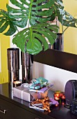 Gifts wrapped in colourful paper and lot tealights on black sideboard next to vase of green artificial leaves