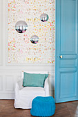 Knit pouffe and white armchair against wainscoting below colourful wallpaper