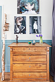 Photos of dolls on wall above old wooden chest of drawers