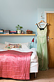 Dress on clothes hanger hung from peg next to bed with pink quilt