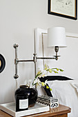 Articulated wall-mounted lamp above black and white ornaments on bedside table