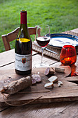Salami and cheese on wooden board and bottle of wine on table in garden