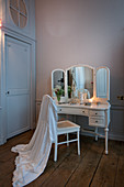 White dressing gown hung over chair in front of antique dressing table