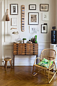 Rattan chair and chest of small drawers below gallery of pictures on wall