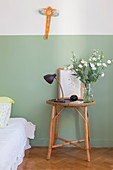 Round, rattan bedside table against two-tone painted wall