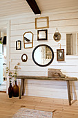 Several mirrors decorating wall above rustic wooden bench in hallway