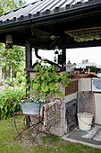 Geraniums on metal stand next to outdoor kitchen with roof and rustic decorations