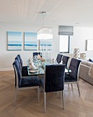 Blue upholstered chairs around dining table in front of seascape paintings on wall in open-plan interior