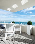 White outdoor furniture on balcony with glass balustrade and sea view