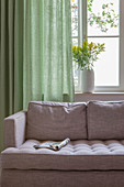 Magazine on grey sofa in front of window with green curtain