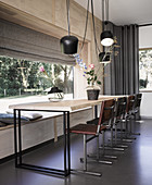 Long dining table, chairs and pendant lamps next to panoramic window