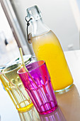 Pink and yellow drinking glasses in front of bottle of pop