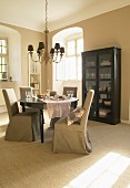 Beige loose-covered chairs and black display cabinet in elegant dining area