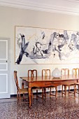 Long exotic-wood table and chairs below modern paintings in historical interior