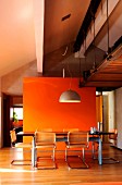 Dining table in front of orange wall below industrial-style gallery