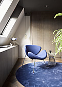 Blauer Designerstuhl auf rundem blauem Teppich unterm Dachfenster