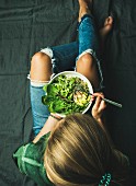 Person isst vegane grüne Power-Bowl mit Spinat, Rucola und Avocado