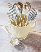 Silver forks and spoons in retro milk jug on rustic wooden table