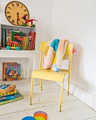 Patchwork knitted blanket on yellow chair and vintage toys in child's bedroom