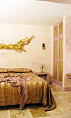 Doppelbett mit goldfarbener Tagesdecke, darüber goldfarbene, kunsthandwerkliche Dekoration im Schlafzimmer
