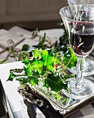 Sprig of holly and glasses of red wine on mirrored tray