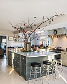 Festively decorated branches in vase on kitchen island with bar stools