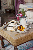 Cups of coffee, coffee pot and pastries on upholstered footstool