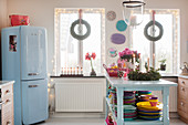 Colourful crockery on island counter and blue fridge in kitchen