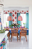 Rattan chairs around brightly set dining table in front of wallpaper with bold floral pattern