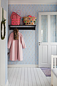 Brightly coloured baskets on coat rack mounted on blue and white diamond-patterned wallpaper