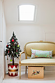 Christmas tree in colourful tub and Baroque couch below skylight