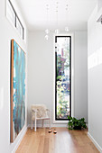 Bright hallway with armrest chair in front of a narrow window, turquoise picture on the wall