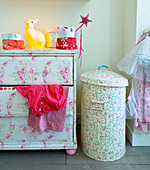 Revamped furnishings in child's bedroom: old chest of drawers and metal bin covered with floral wallpaper