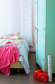 Floral bedlinen on bed, floral wallpaper and mint-green wardrobe