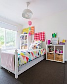 Wooden bed with colorful bedding in girl's room with white walls