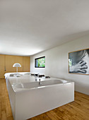 Bathtub in white block and bed in combined bedroom and bathroom
